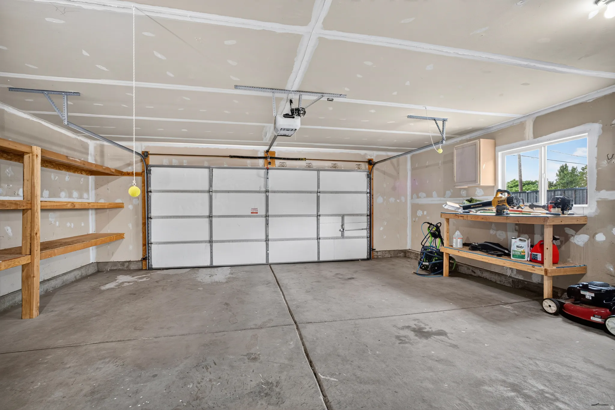 Attached garage featuring a concrete floor, overhead garage door, built-in shelving, and a window