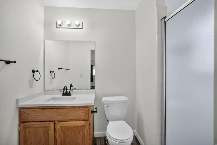 Bathroom featuring a wood-finish vanity with an integrated sink and white countertop, black fixtures, and a shower with a frosted glass enclosure
