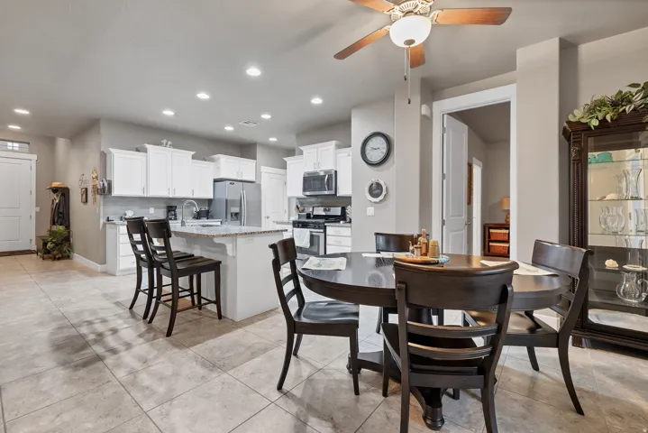 Open-concept kitchen and dining area featuring tile flooring, white cabinetry, a kitchen island with seating, recessed lighting, and a ceiling fan