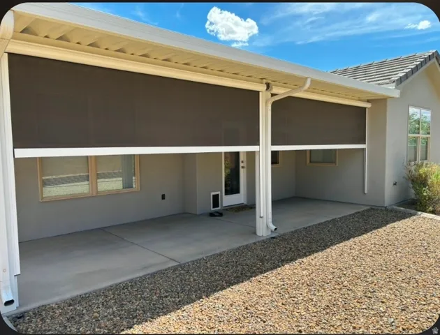 Covered patio with retractable screens, concrete slab, stucco exterior, and rock landscaping