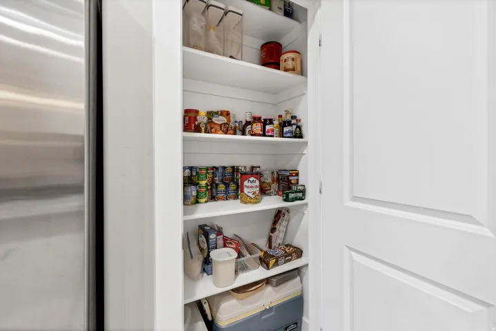 Built-in pantry with multiple white shelves, paneled door, and adjacent stainless steel appliance