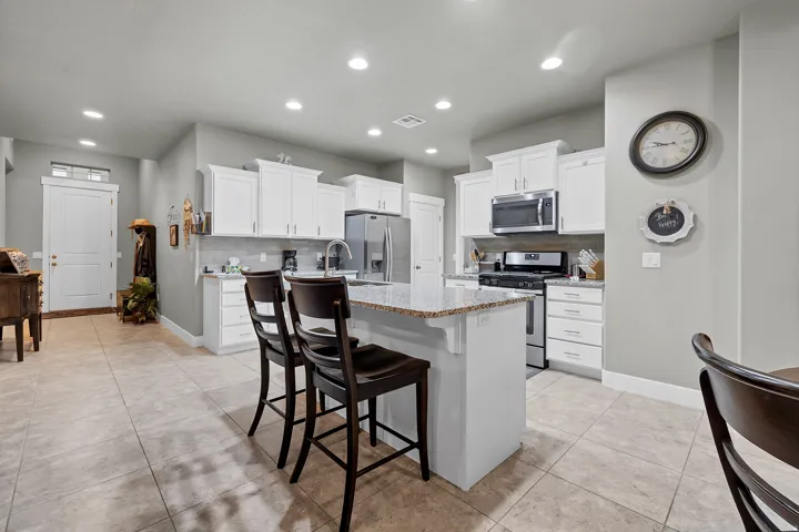 Kitchen featuring white cabinetry, stainless steel appliances, a center island with seating, granite countertops, and tile flooring