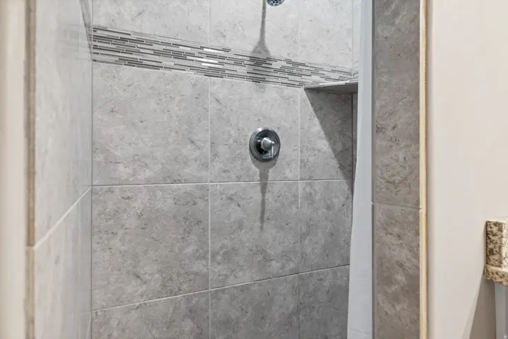 Tiled shower enclosure featuring a mosaic accent band, recessed shelf, and a chrome shower fixture