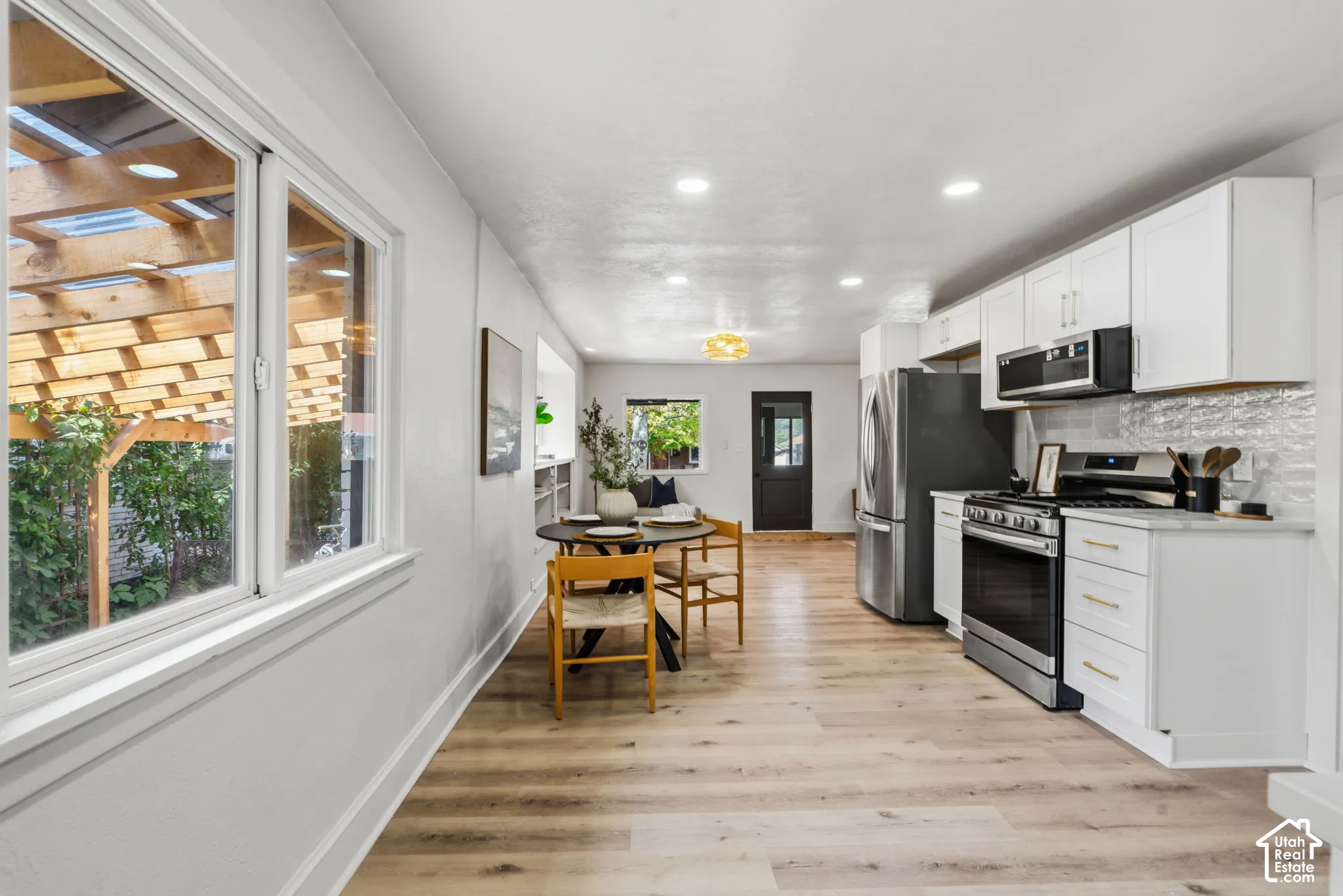Wood-finish flooring throughout, white cabinetry with gold-tone hardware, stainless steel appliances, white subway tile backsplash, and recessed lighting