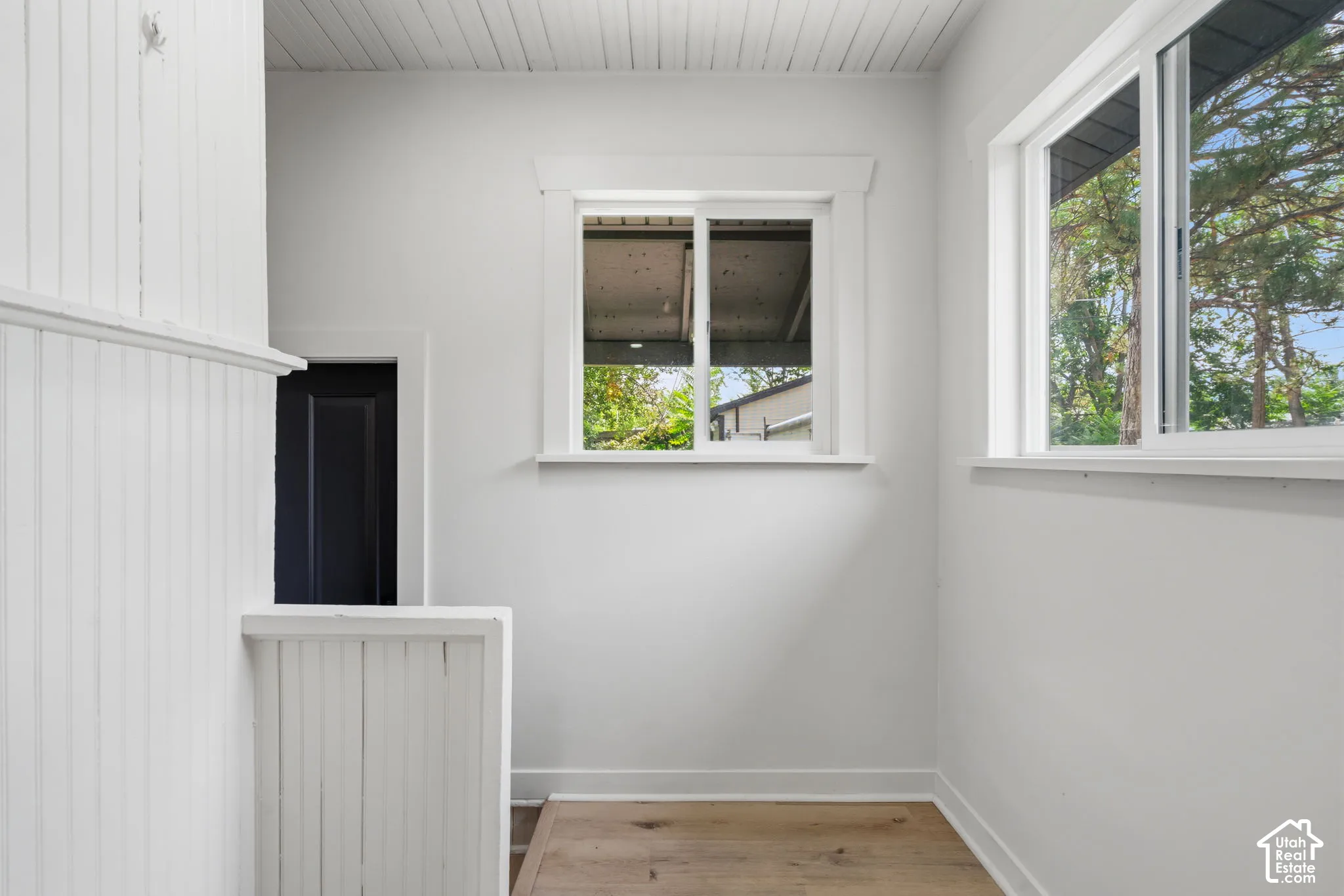 Wood-finish flooring, beadboard wall paneling, two windows with white trim, and a wood-paneled ceiling