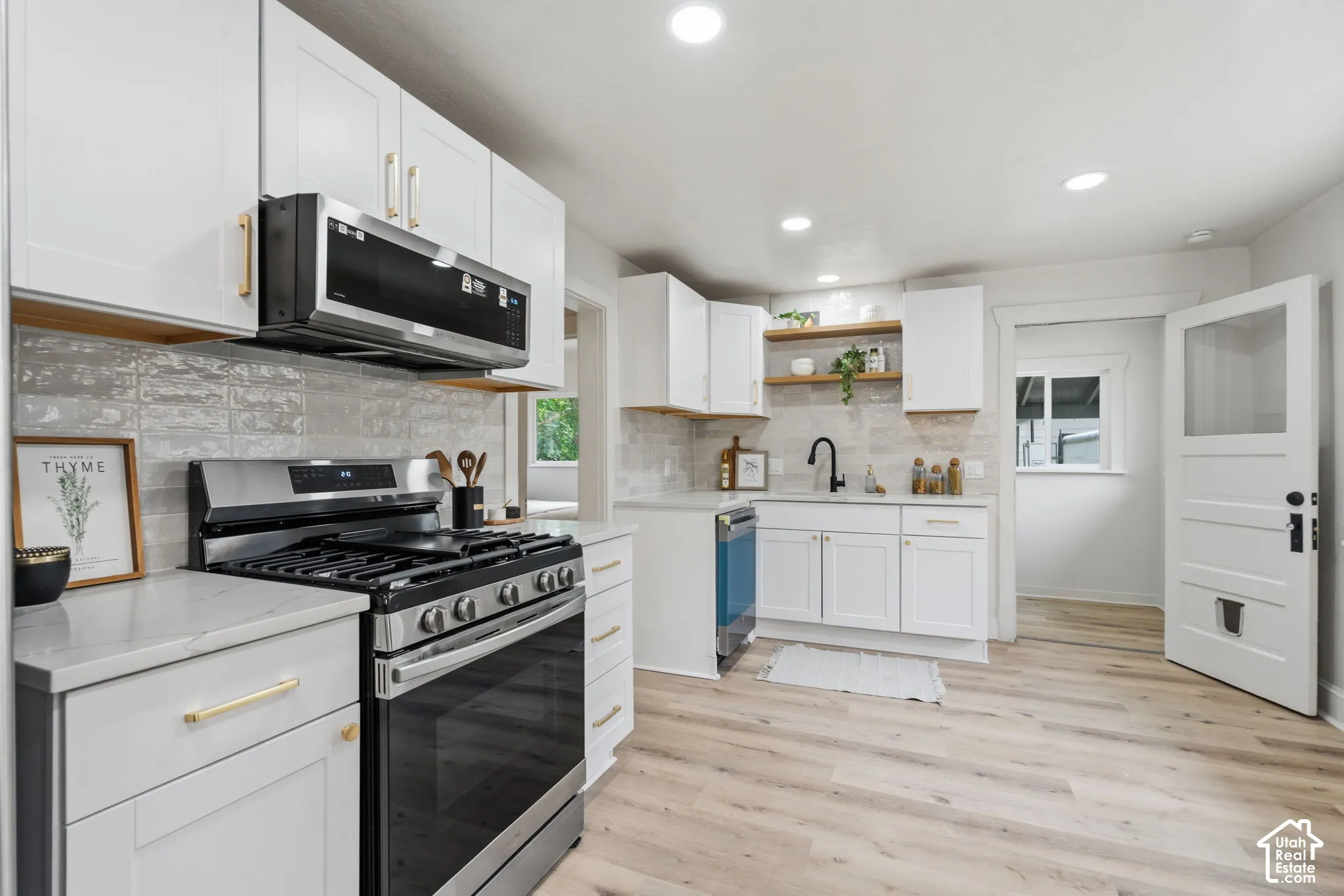 Modern kitchen featuring white cabinetry, stainless steel appliances, wood-finish flooring, recessed lighting, and open shelving