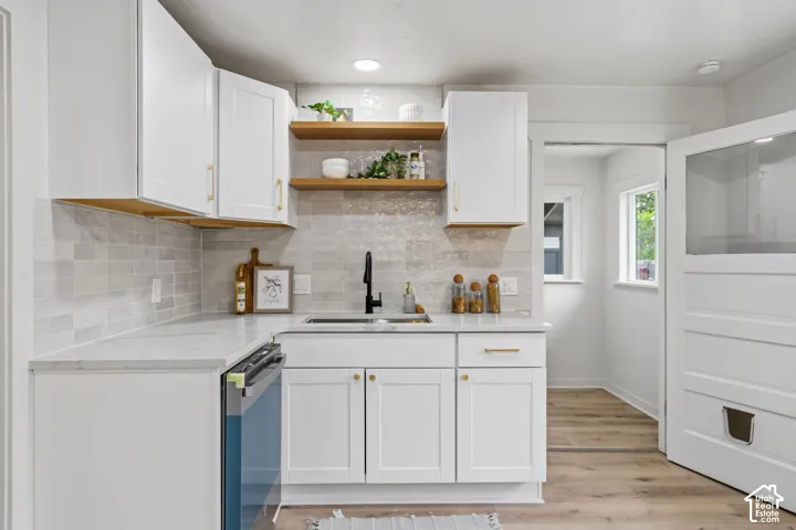 White shaker cabinetry with gold-tone hardware, grey subway tile backsplash, white countertops, wood-finish flooring, and open shelving