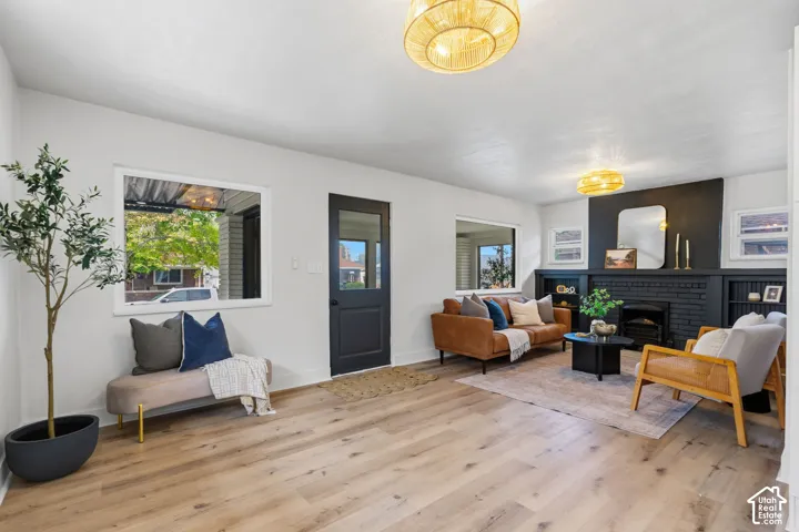 Wood-finish flooring throughout, multiple windows providing natural light, a dark-painted fireplace with integrated shelving, and two woven ceiling light fixtures