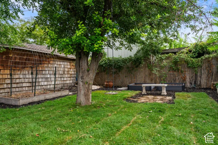 Expansive grassy yard featuring a mature tree, two raised garden beds, and a stone patio area