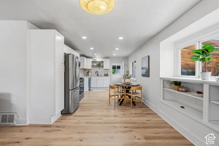 Open-concept kitchen with white cabinetry and stainless steel appliances, wood-finish flooring, recessed lighting, and built-in shelving below a large window