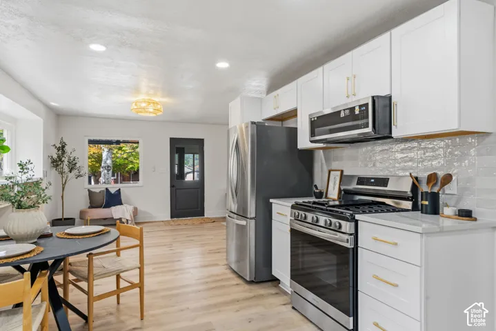 Open-concept kitchen with stainless steel appliances, white cabinetry, and light wood-finish flooring