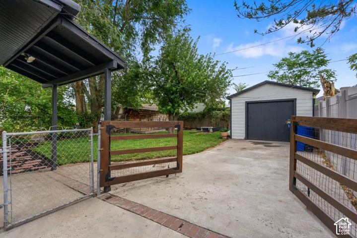Detached garage with a dark-toned door, concrete driveway, and covered patio area with a chain-link fence