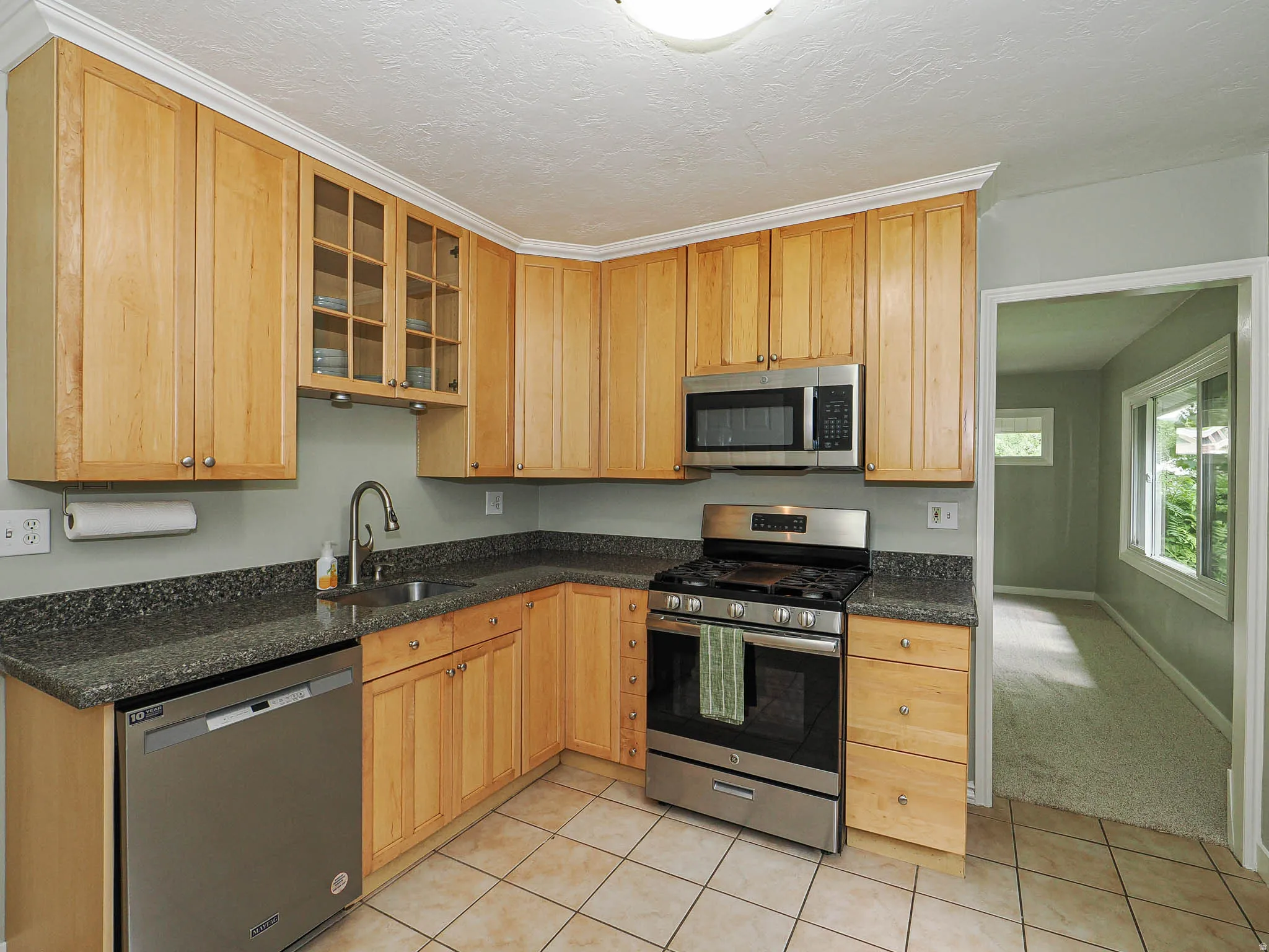 Updated wood cabinetry with glass-front upper storage, stainless steel appliances, speckled dark countertops, and tile flooring