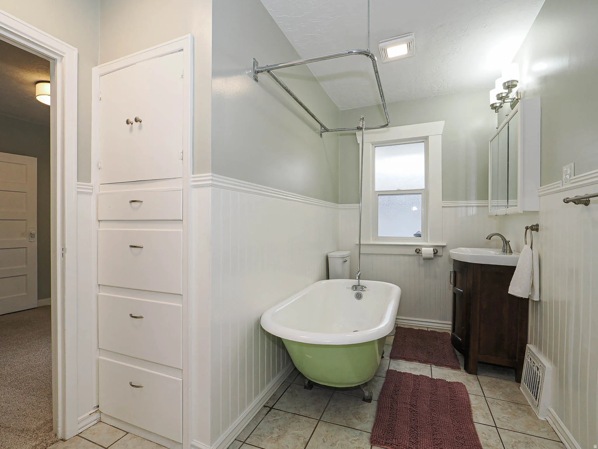 Spa-inspired primary bathroom featuring a freestanding soaking tub with polished chrome fixtures, subway tile wainscoting, pedestal sink with dark wood vanity base, large frameless glass shower enclosure, recessed and sconce lighting, and tile flooring th