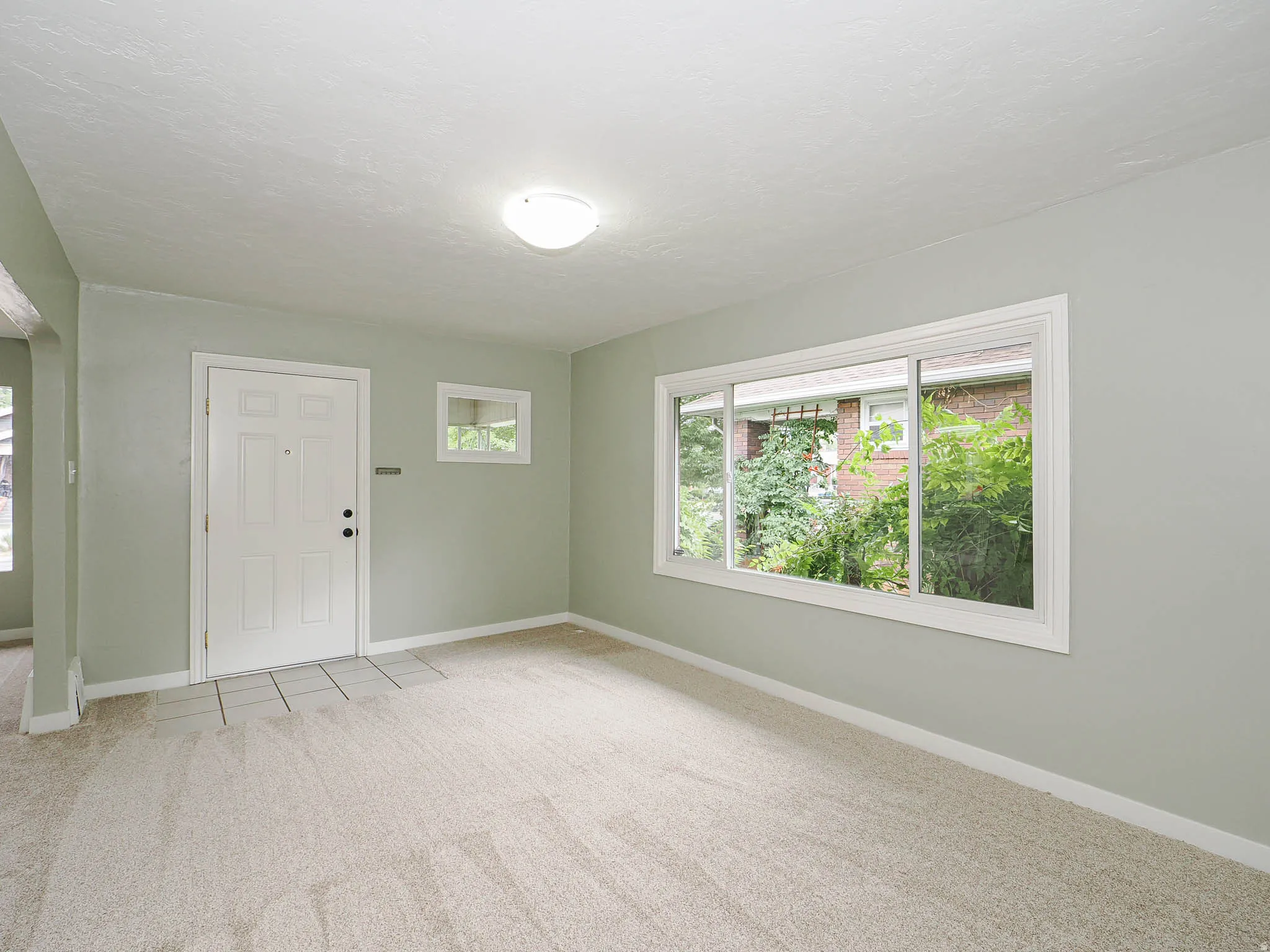 Bright and airy entry room showcasing sage-green walls, new carpet, and abundant natural light from expansive  windows