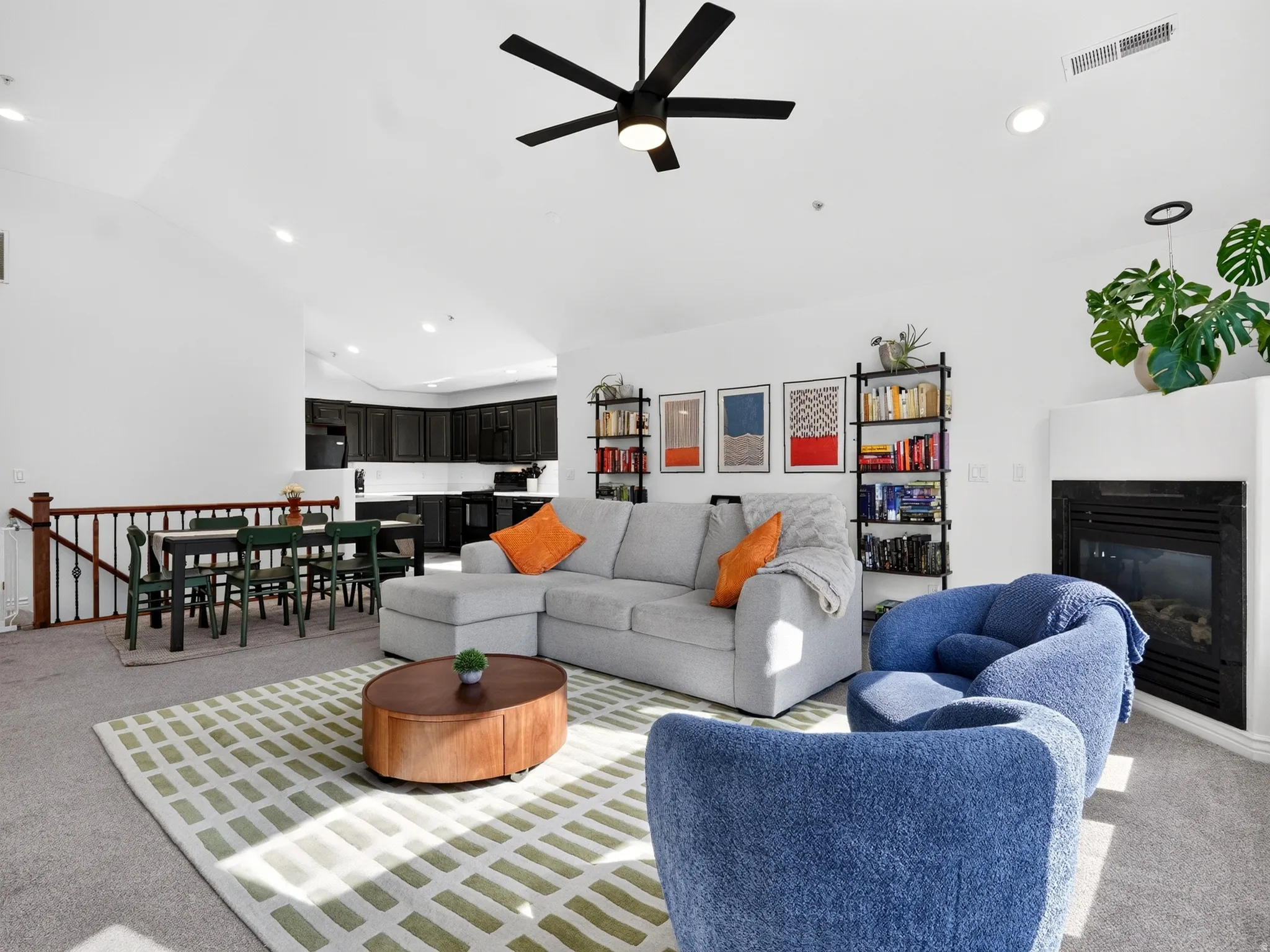 Open-concept living space featuring a gray upholstered sectional, wood-finish coffee table, geometric area rug, and ceiling fan