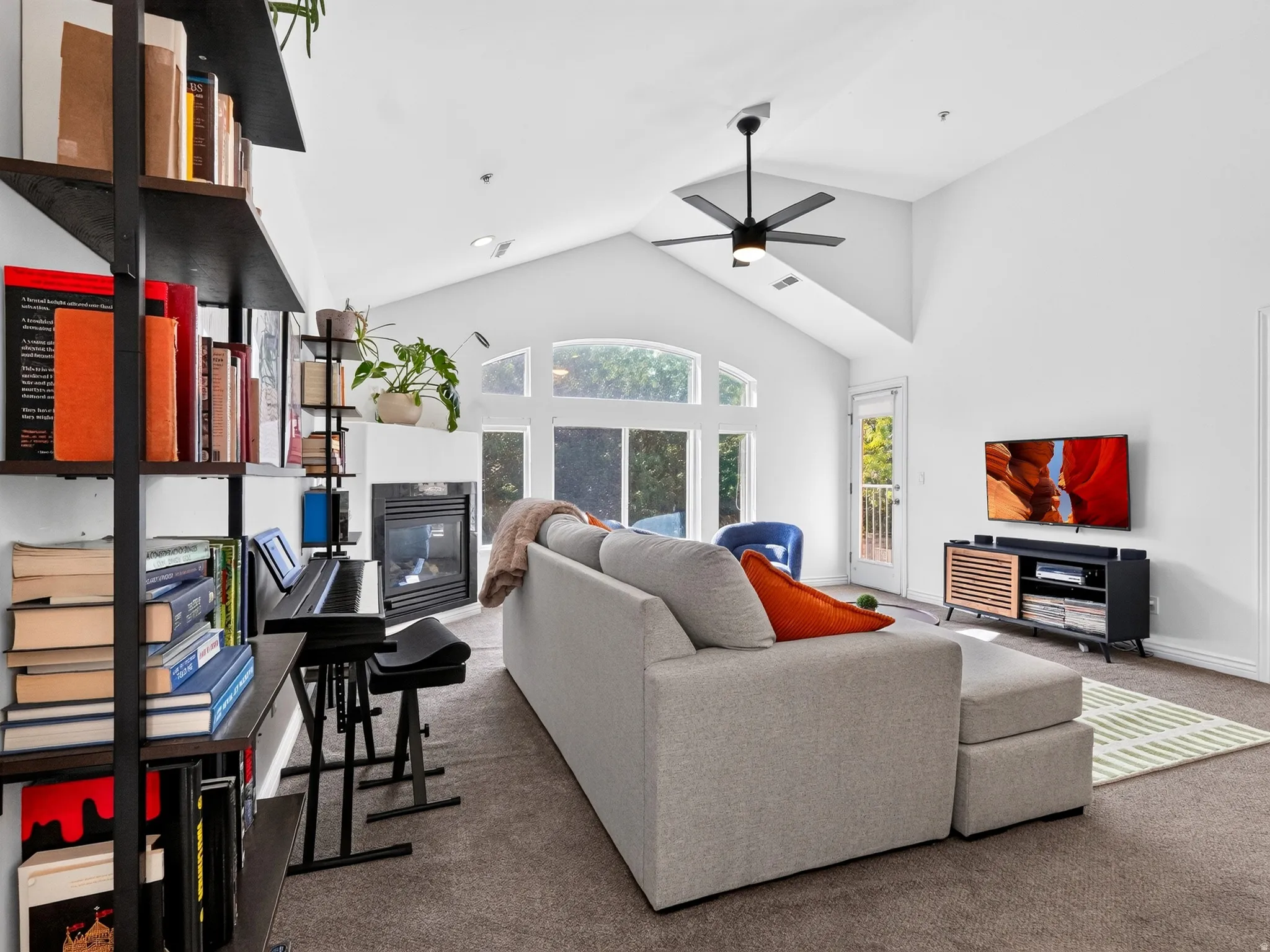 Bright, open-concept living space featuring vaulted ceilings with ceiling fan, abundant natural light from arched windows, and a fireplace
