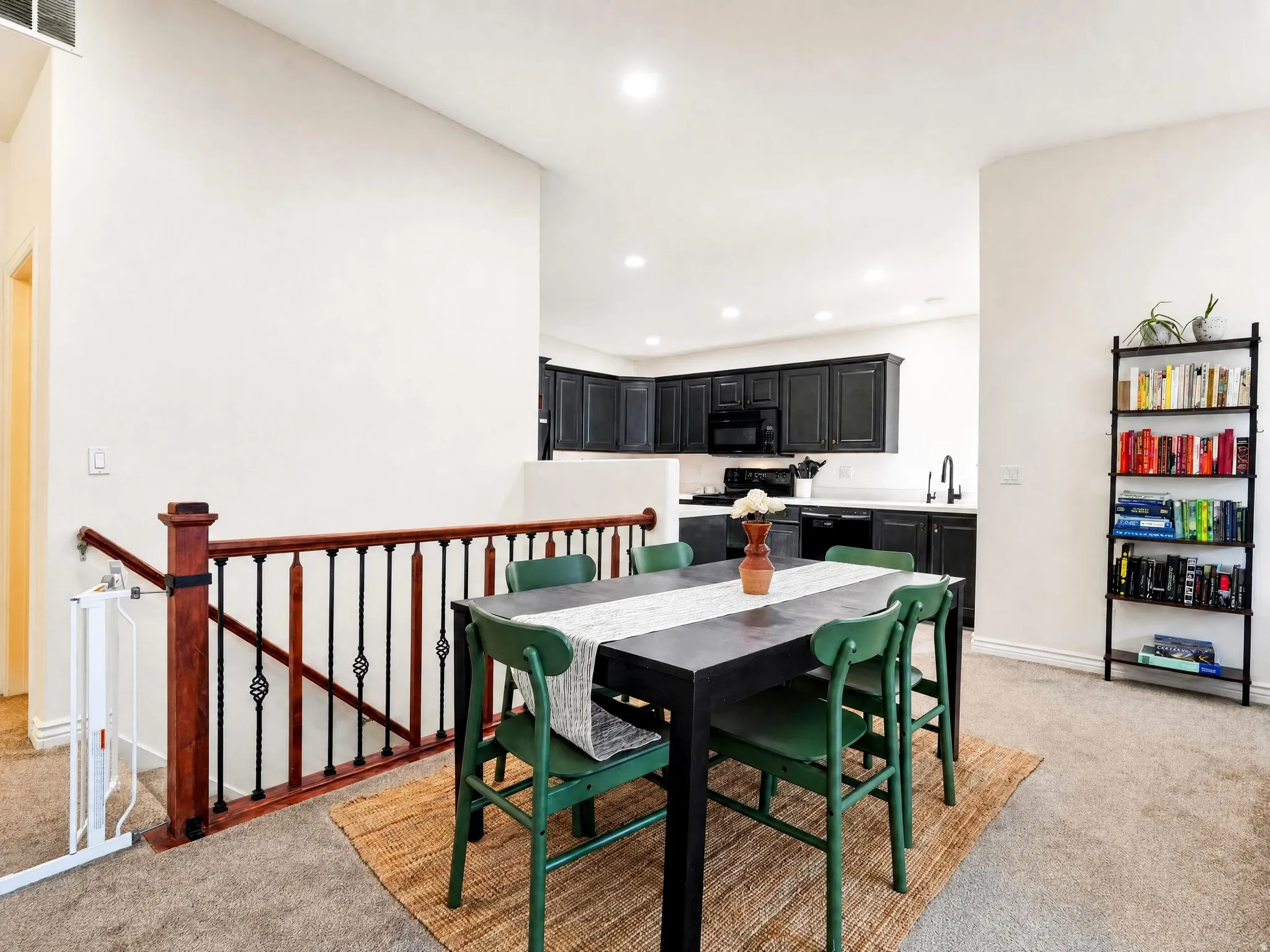 Open-concept living space featuring a black dining table with green upholstered chairs, dark cabinetry with stainless steel appliances, recessed ceiling lighting, and polished concrete flooring throughout