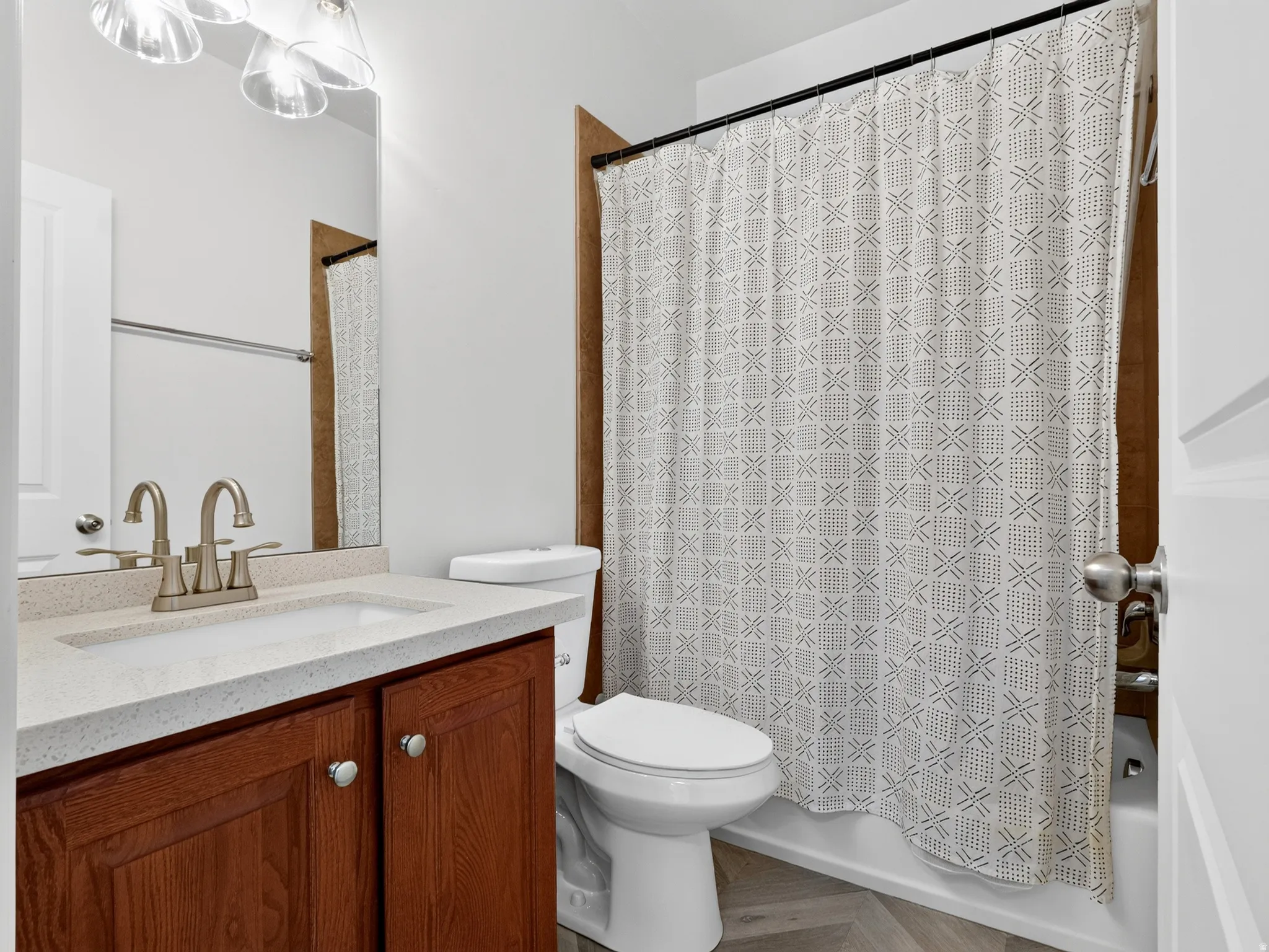 Spa-inspired bathroom featuring a wood-finish vanity with dual-handle brushed nickel faucet, white marble-look countertop, and recessed lighting