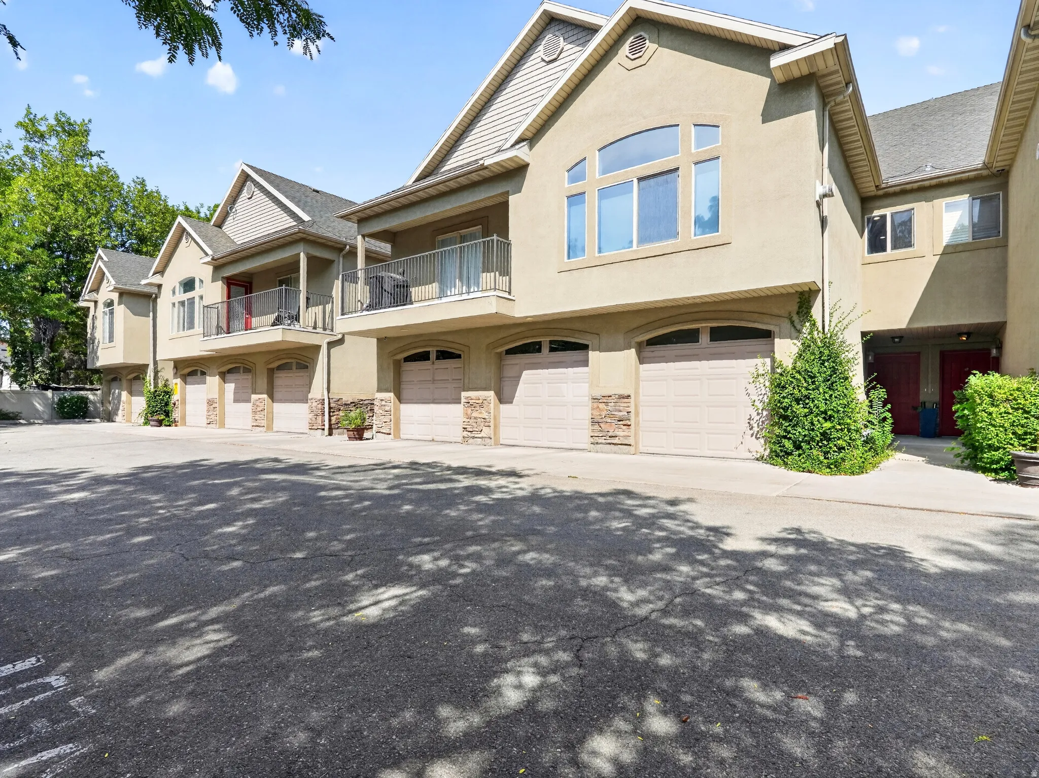 Elegant residential complex featuring multiple attached townhomes with cream-colored stucco exterior, stone accents, and pitched rooflines