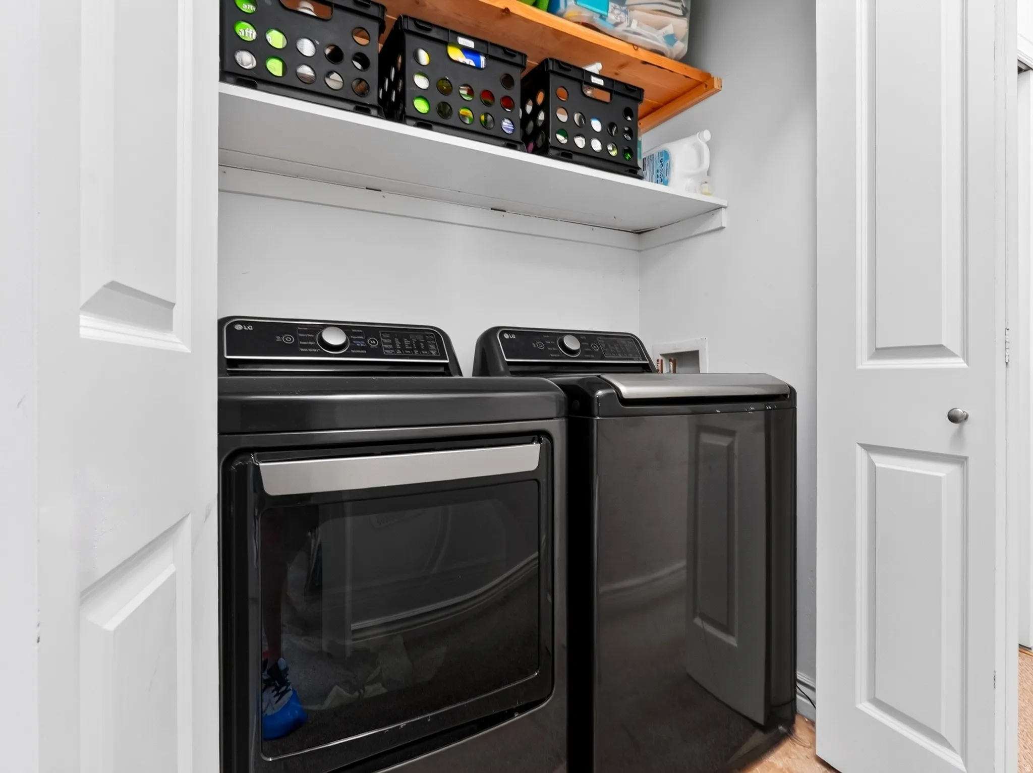 Dedicated laundry room featuring side-by-side black front-load washer and dryer with digital control panels, positioned beneath white floating shelving