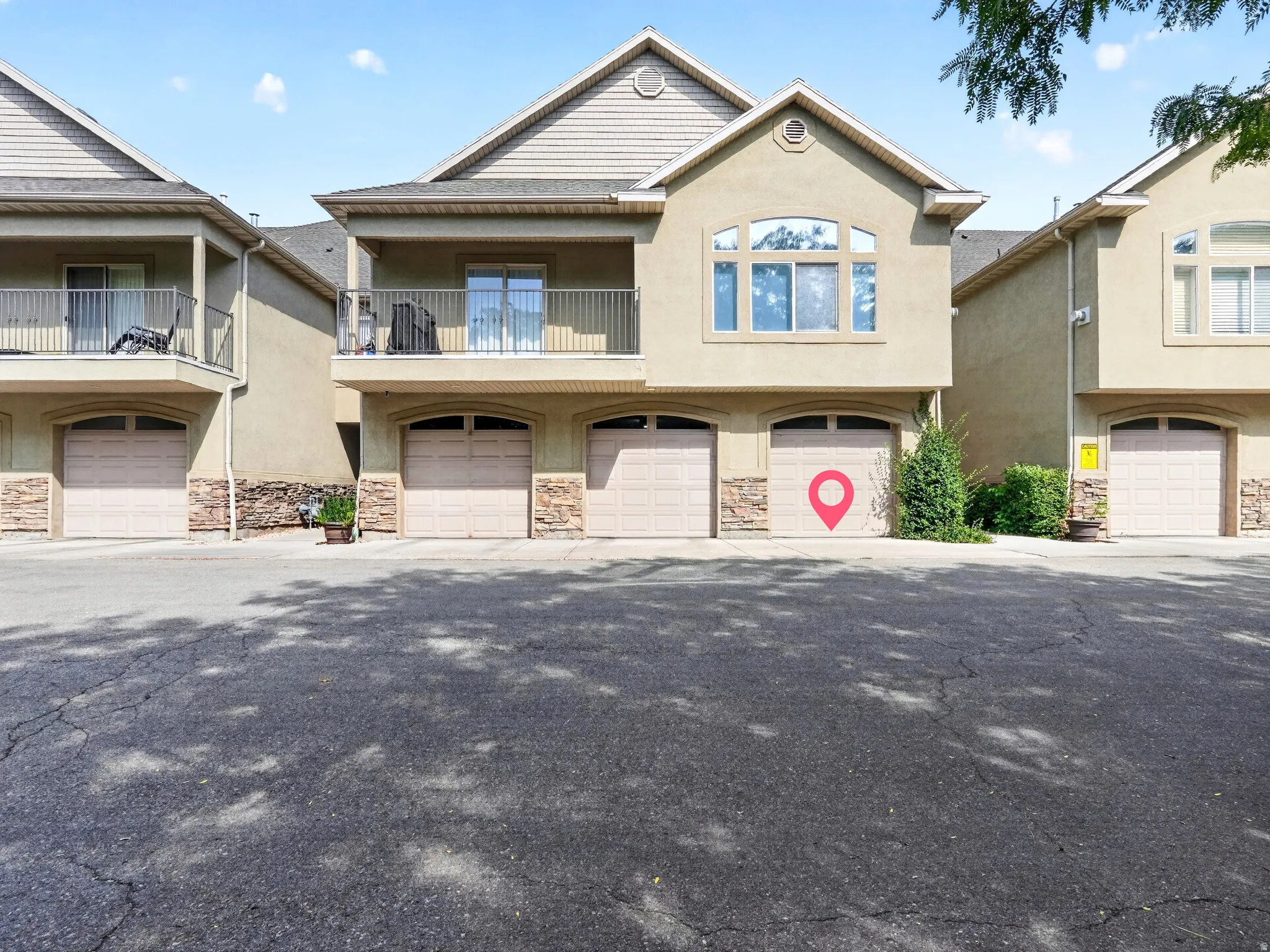 Stunning two-story residence featuring a tan and stone exterior with multiple two-car garage bays, arched roofline details, and upper-level windows with decorative trim