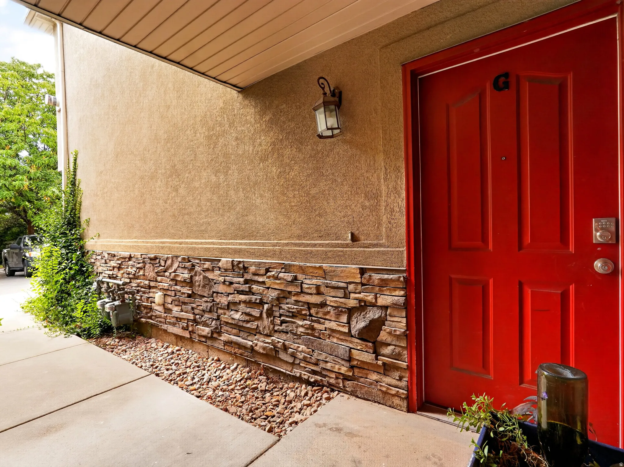 Welcoming entry featuring a bold red six-panel door with satin nickel hardware, complemented by stucco-finished upper walls and a decorative stone veneer base