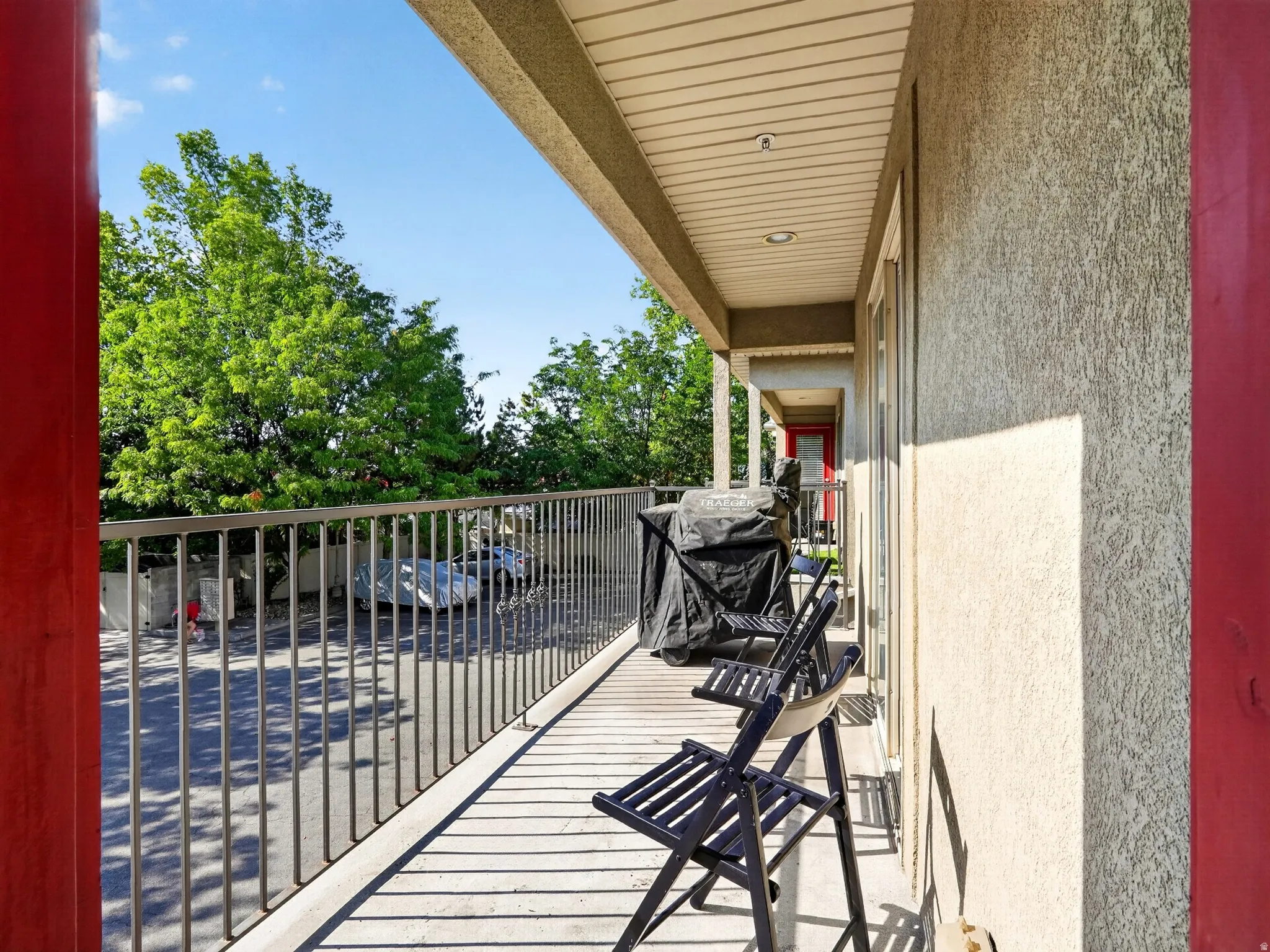 Covered balcony with metal railing, wood-finish decking, and mature tree backdrop
