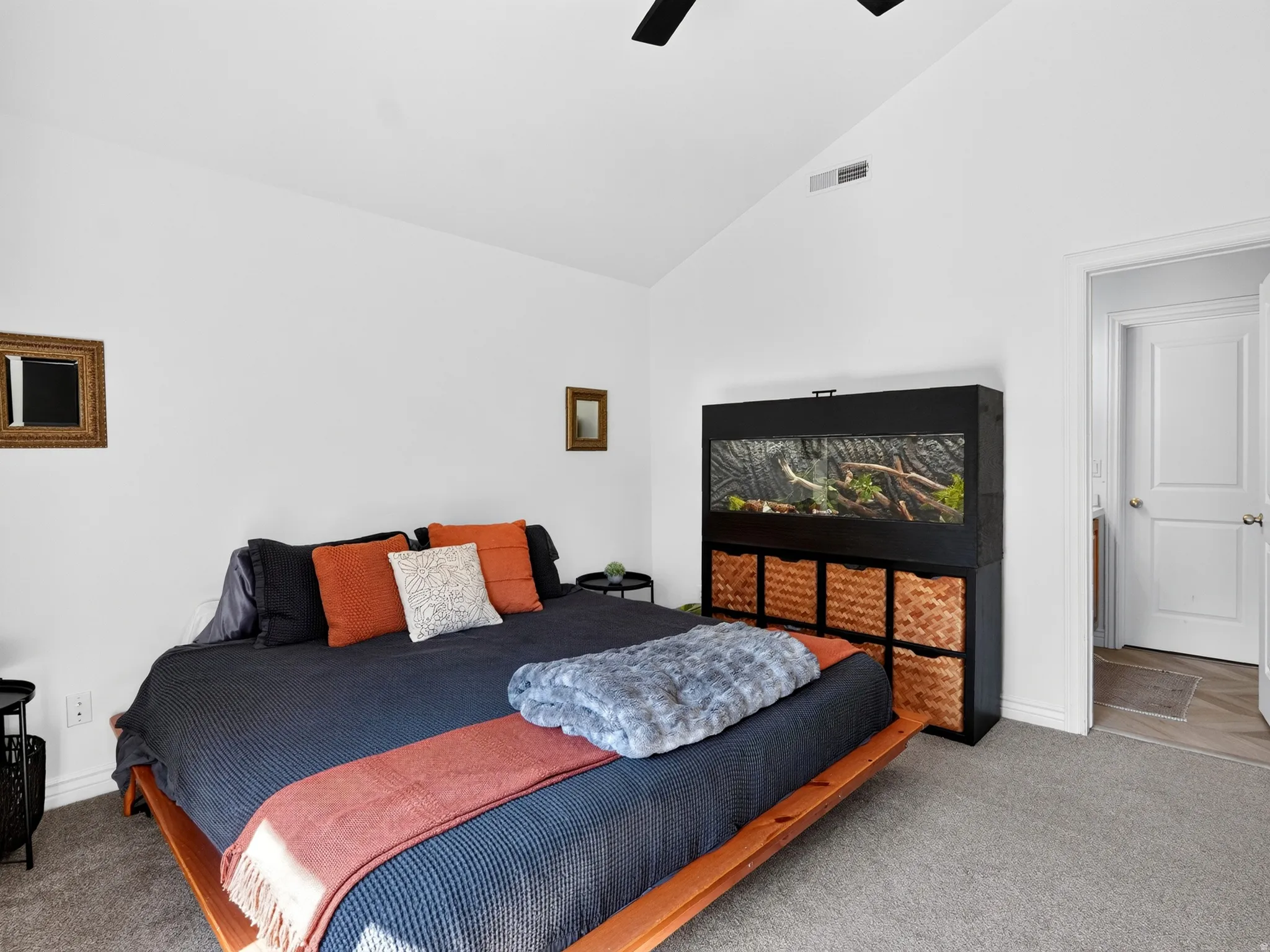Spacious secondary bedroom featuring a wood-finish platform bed frame with integrated storage, carpet flooring, and built-in media console with woven storage baskets