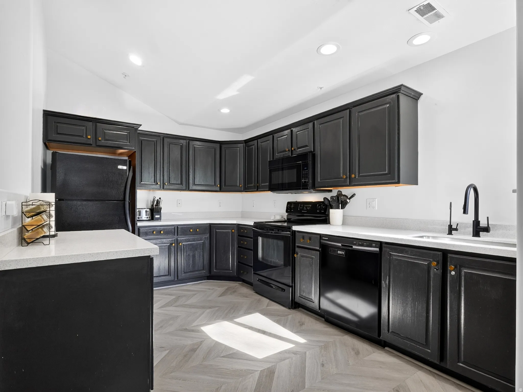 Modern kitchen featuring dark cabinetry with brushed gold hardware, white quartz countertops, and a large center island with waterfall edge