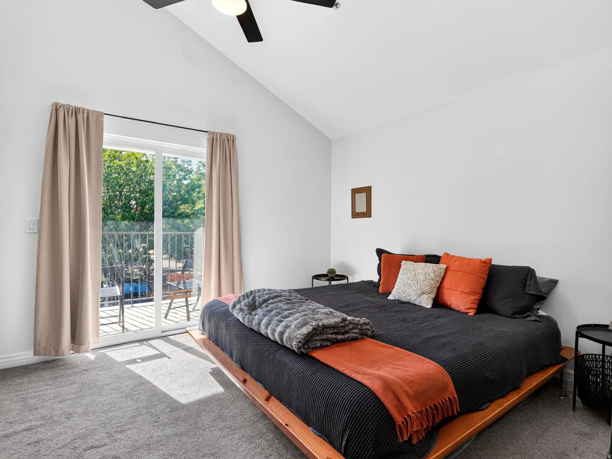 Bright secondary bedroom featuring vaulted ceilings with ceiling fan, sliding glass doors opening to a private balcony with metal railing, neutral wall finishes, and wood-finish flooring throughout
