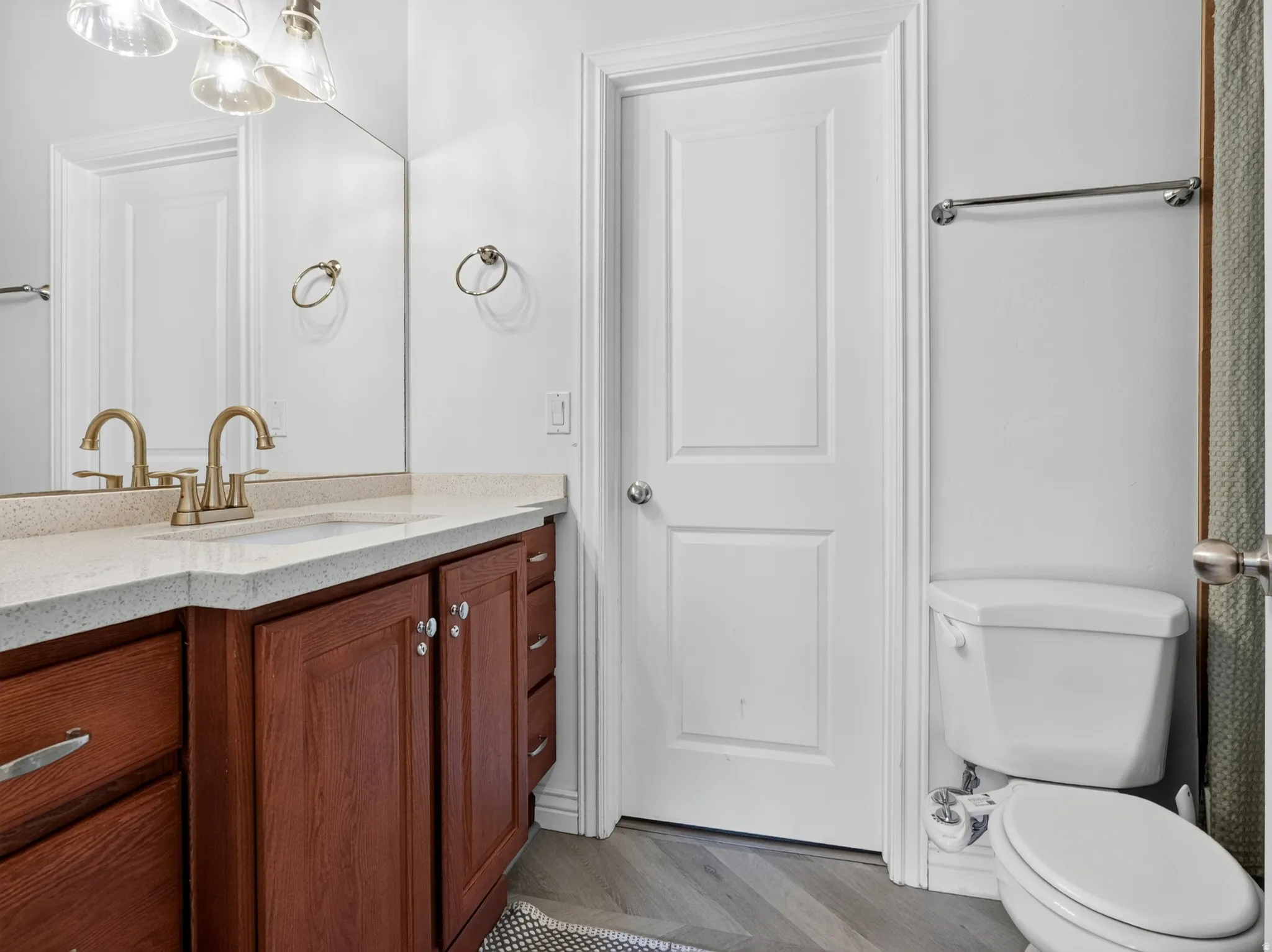 Elegant bathroom featuring a rich wood-finish vanity with dual brass faucets, white marble-look countertop, and a large framed mirror with integrated lighting