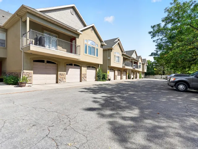 Townhome community featuring multiple attached units with two-car garages, stone and siding exterior finishes, second-story balconies with metal railings, and mature landscaping throughout the shared grounds