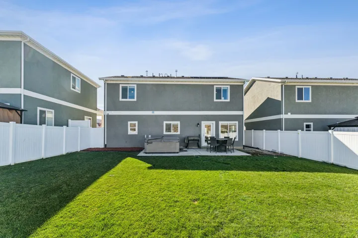 Expansive grassy yard with white privacy fencing, a concrete patio, and a hot tub