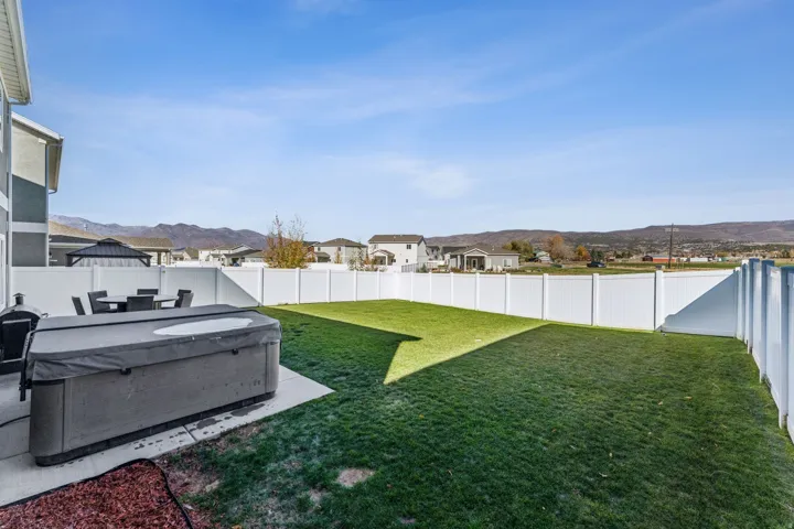 Expansive backyard featuring a manicured lawn, a white privacy fence, and a paved patio area