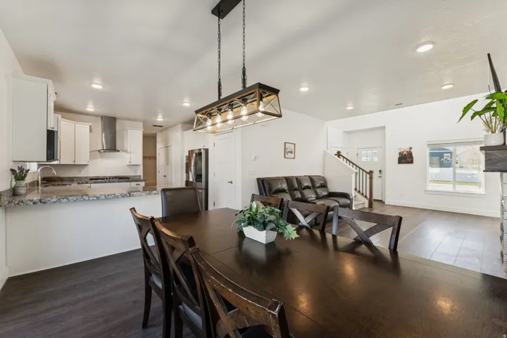 Open-concept living area with wood-finish flooring, recessed lighting, and a kitchen featuring white cabinetry, stainless steel appliances, and a granite-style countertop