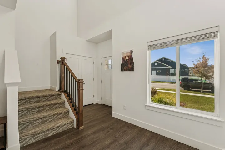 Vaulted entry ceiling, wood-finish flooring, staircase with wood newel posts and metal spindles, large window with blinds, and white panel doors