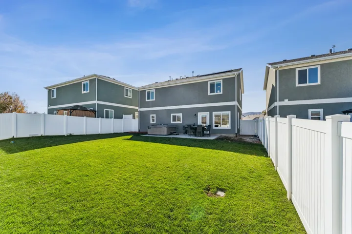 Expansive green lawn with a white vinyl privacy fence, a concrete patio, and an outdoor spa