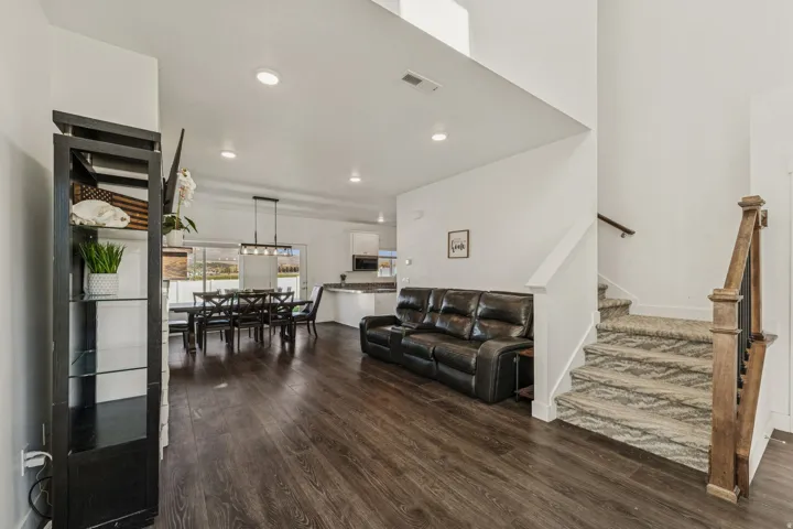 Vaulted ceilings, wood-finish flooring, a contemporary staircase with wood railing, recessed lighting, and a dining area with an overhead linear light fixture