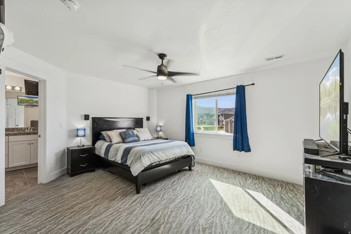 Spacious room with patterned carpeting, a large window, and an attached bathroom featuring a dual-sink vanity with a granite-style countertop