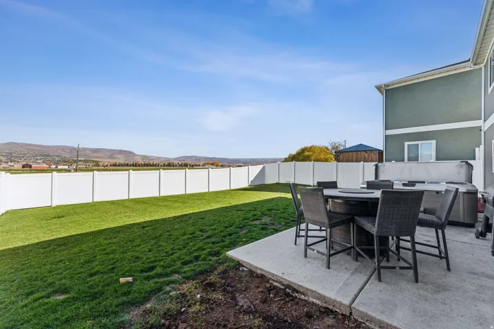 Expansive lawn area, concrete patio, white privacy fencing, and mountain backdrop