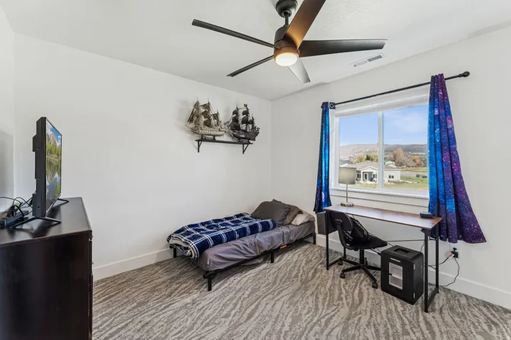 White walls with textured carpet flooring, large window with ample natural light, and a ceiling fan