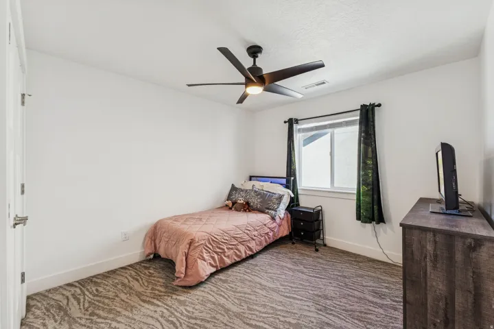 Window with natural light, textured carpet, white walls, black ceiling fan, wood-finish dresser