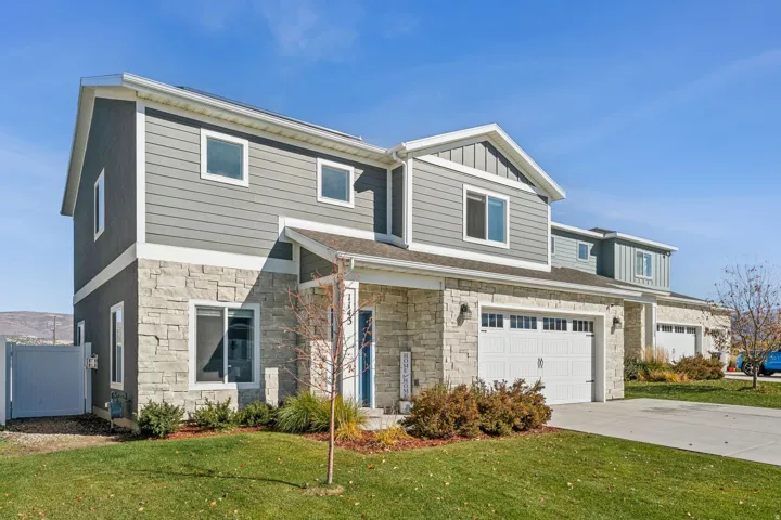 Exterior featuring gray horizontal siding, stone veneer accents, white trim, a gabled roofline, and an attached two-car garage