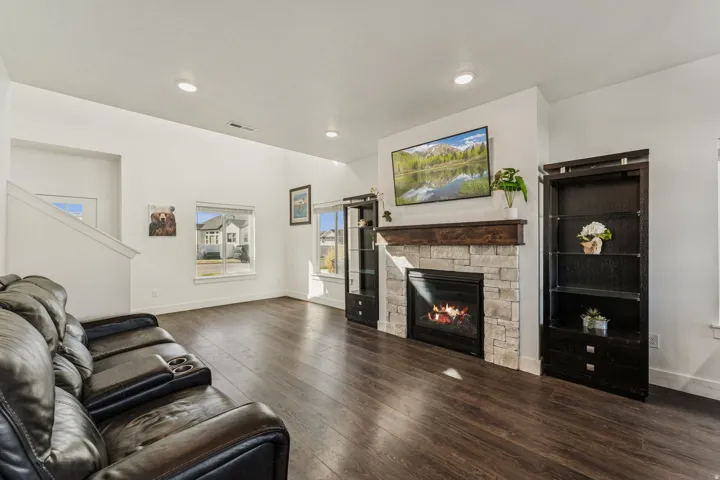 Spacious living area featuring dark wood-finish flooring, a stone-clad fireplace with a wood mantle, and recessed lighting