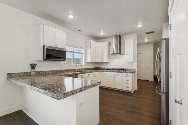 Modern kitchen featuring white cabinetry, granite countertops, stainless steel appliances, dark wood-finish flooring, and recessed lighting