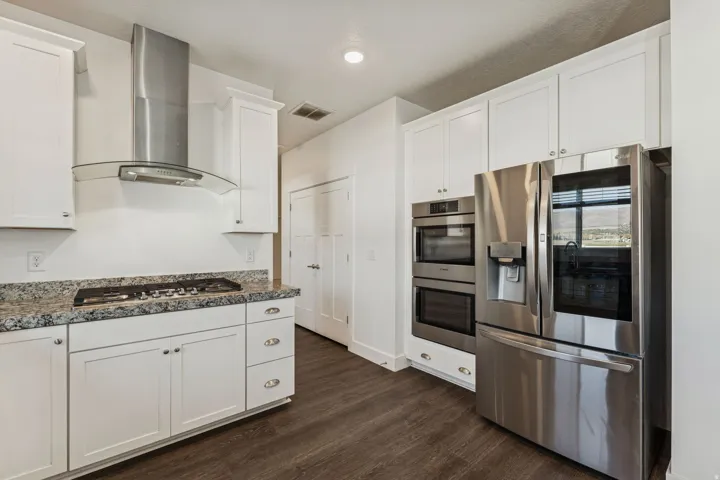 White cabinetry, integrated stainless steel appliances, dark wood-finish flooring, and light-toned countertops