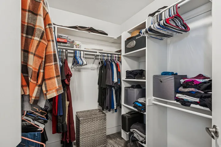 Walk-in closet featuring built-in shelving, multiple hanging rods, and wood-finish flooring