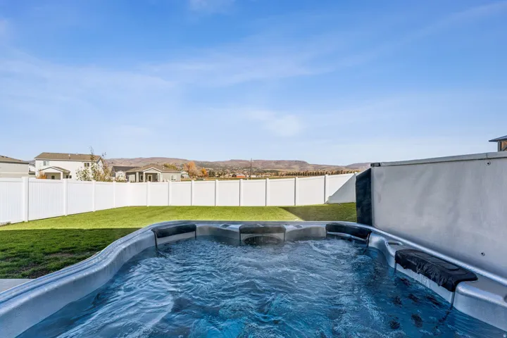 Outdoor hot tub, expansive green lawn, white privacy fencing, and distant mountain scenery