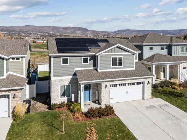Two-story residence featuring a stone and siding exterior, solar panel array, attached two-car garage, and a concrete driveway